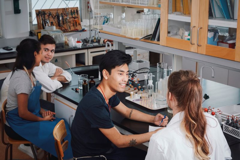 Vier Studenten sitzen sich zugewandt in einem Chemie-Labor.