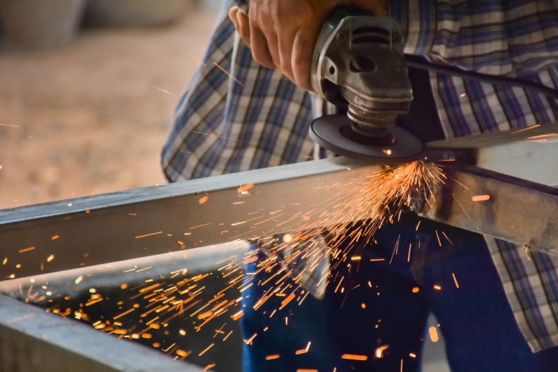 Bildausschnitt einer Frau in einer Werkstatt, die Metall mit einem Schleifer bearbeitet.