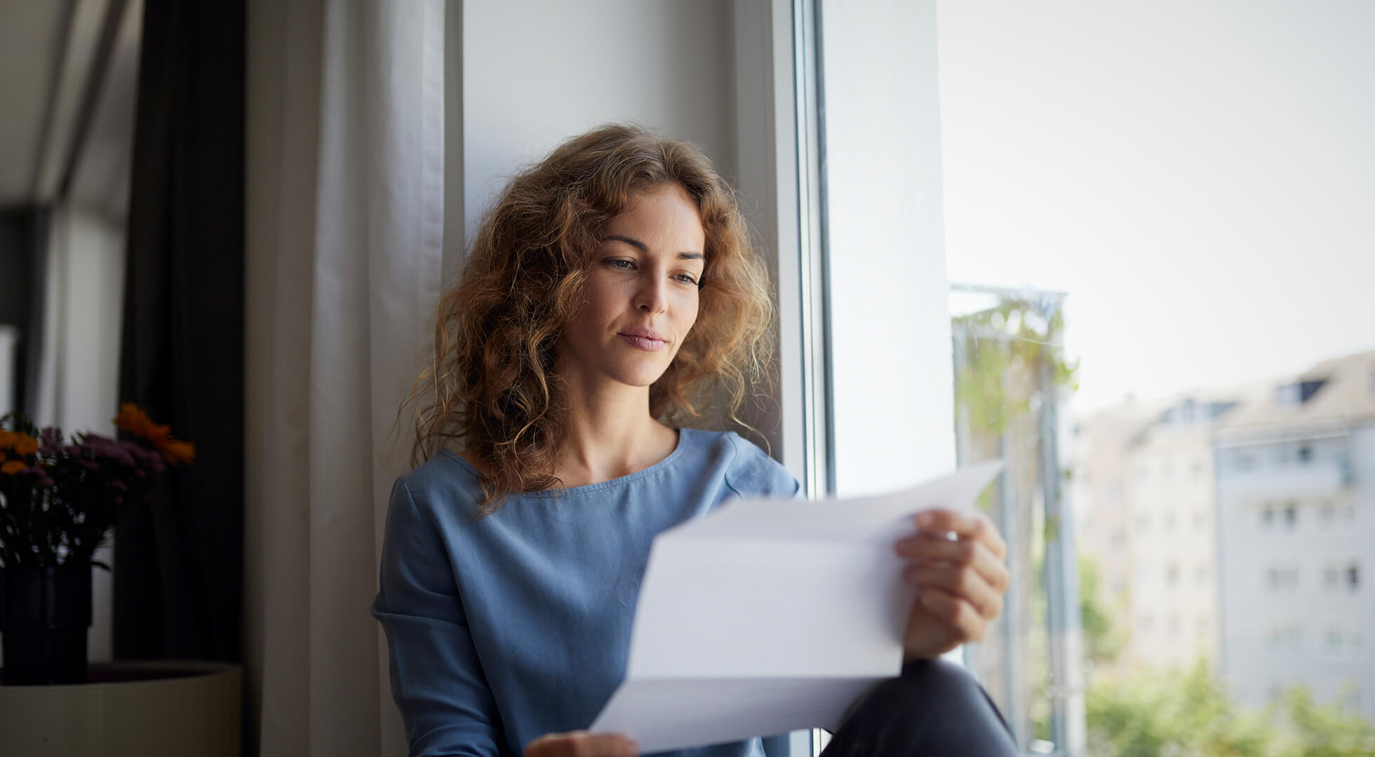 Eine junge Frau liest aufmerksam ein Dokument vor dem Fenster
