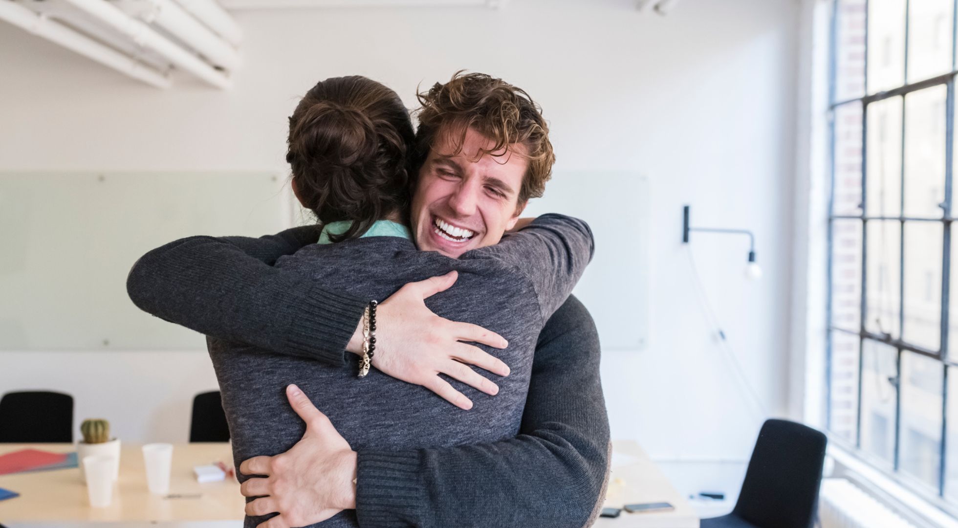 Zwei Menschen umarmen sich, das Gesicht von dem Mann ist sichtbar, er lächelt.