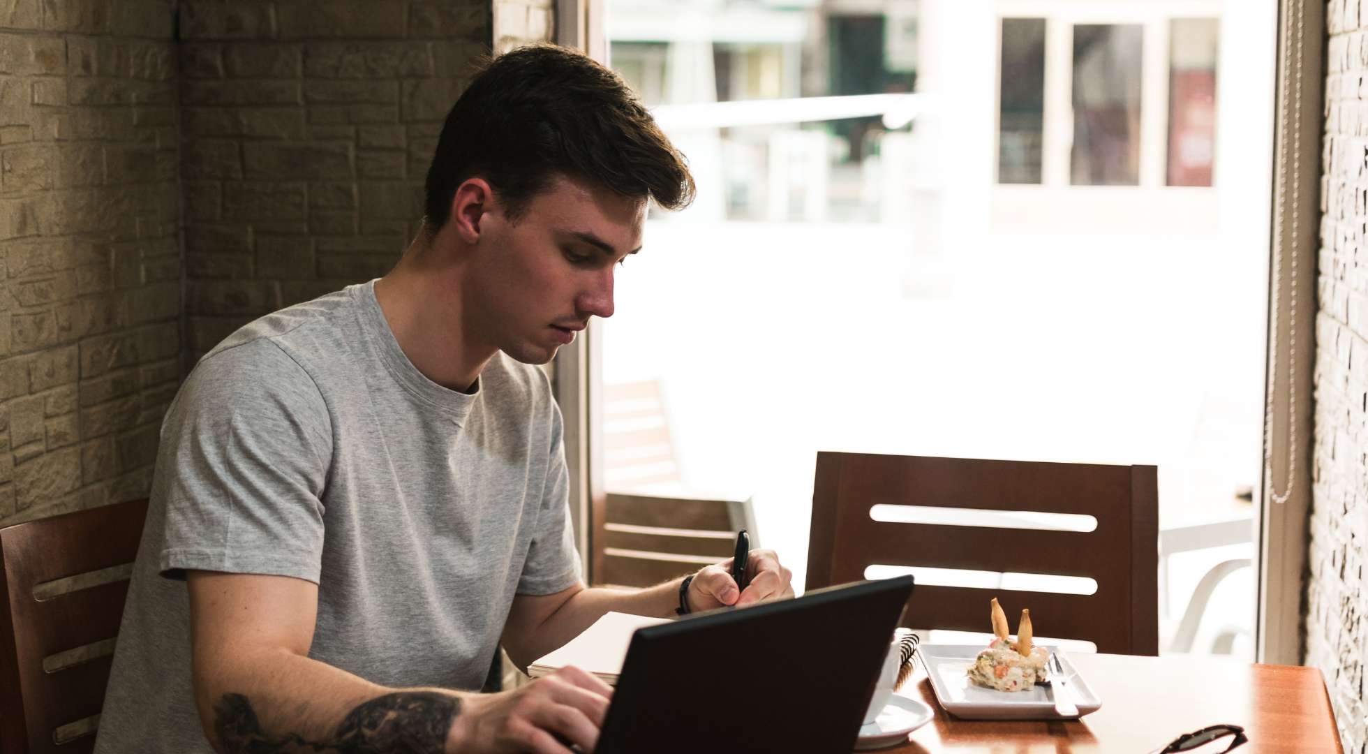 Ein junger Mann in einem Café macht sich Notizen auf einem Notizblock. Auf dem Tisch steht ein Tablet-Computer.