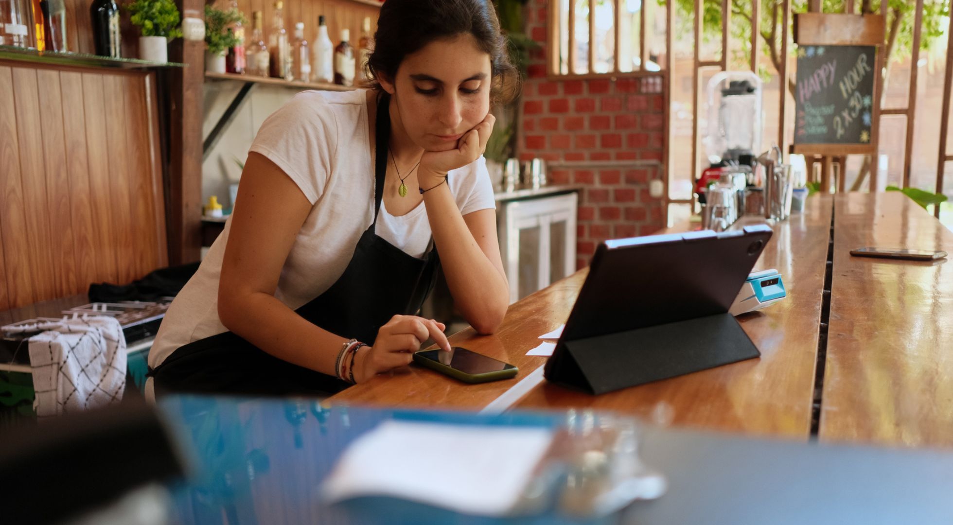 Müde aussehende Kellnerin in einem Café mit Smartphone und Tablet