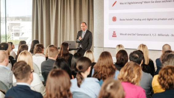 Peter Filzmaier präsentiert in einem Konferenzraum vor einer Gruppe Menschen